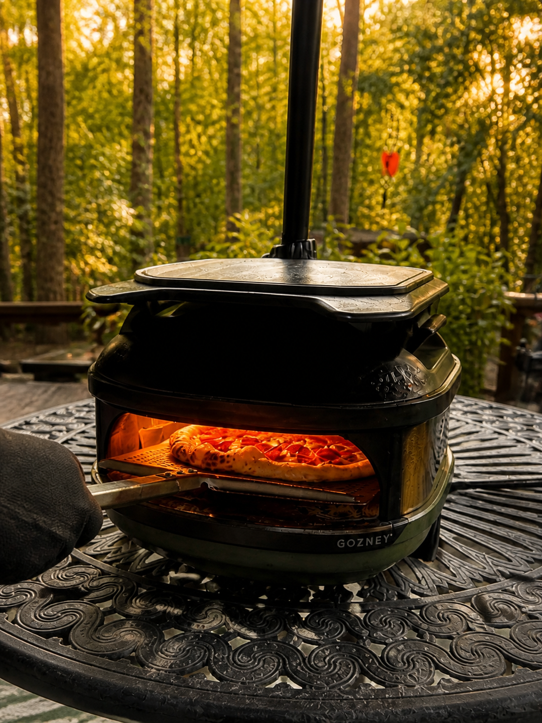A pizza baking in a portable oven in a wooded backyard