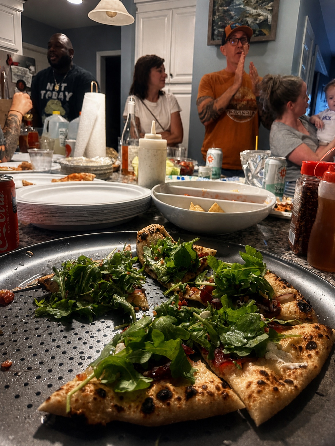 Fresh pizza in the foreground with guests talking in the kitchen