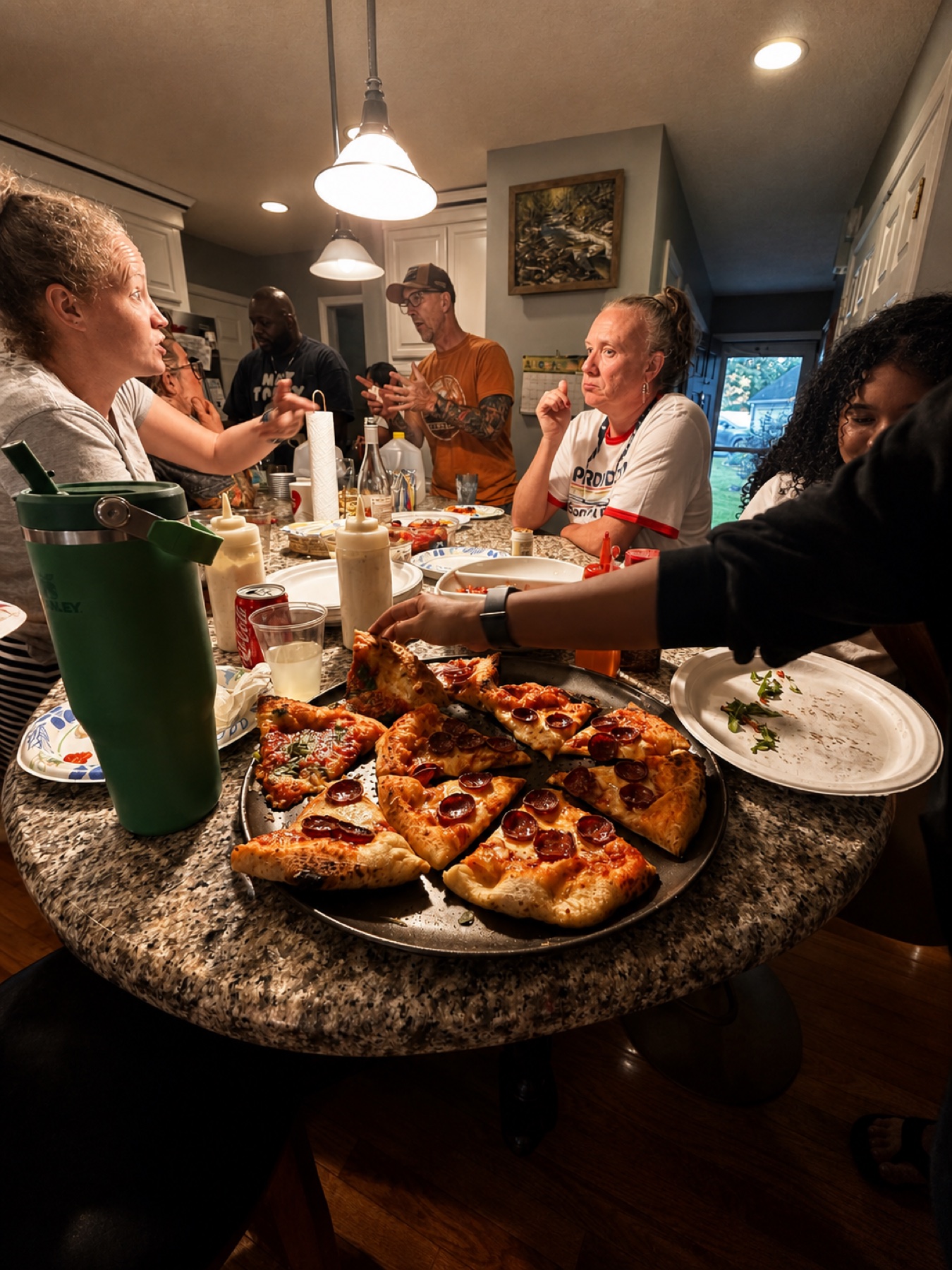 Friends gathering around a kitchen island and reaching for fresh pizza